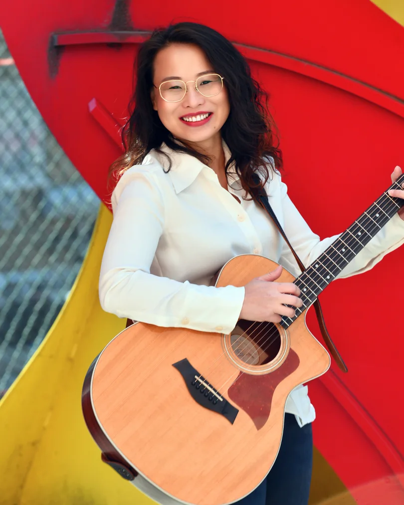 Environmental performer portrait with a guitar and bright red background