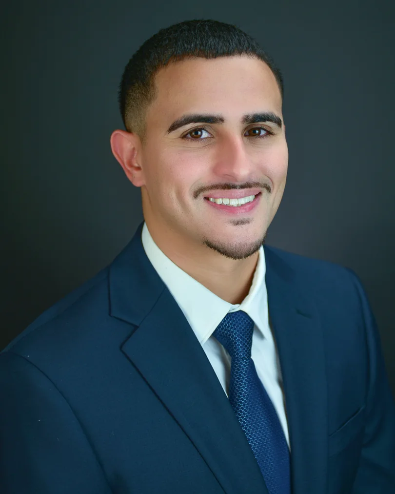 Professional headshot in a blue suit with a dark studio background