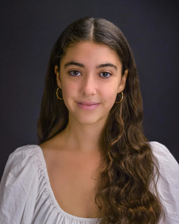 Studio headshot in a white top with a dark background