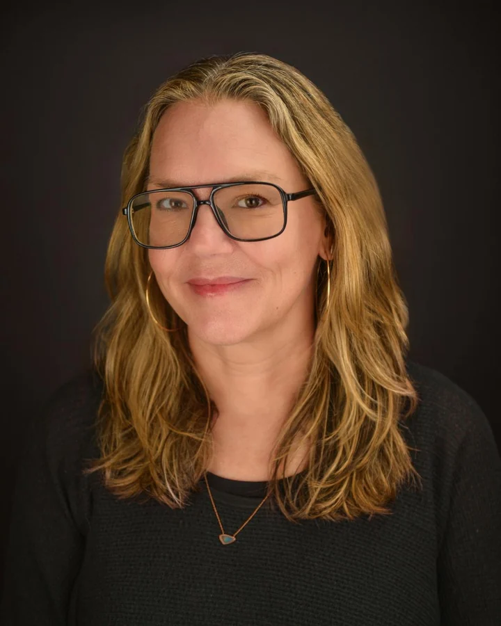 Professional headshot with glasses and a dark studio background