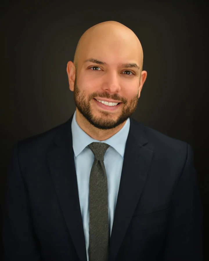 Corporate headshot in a navy suit with a dark studio background