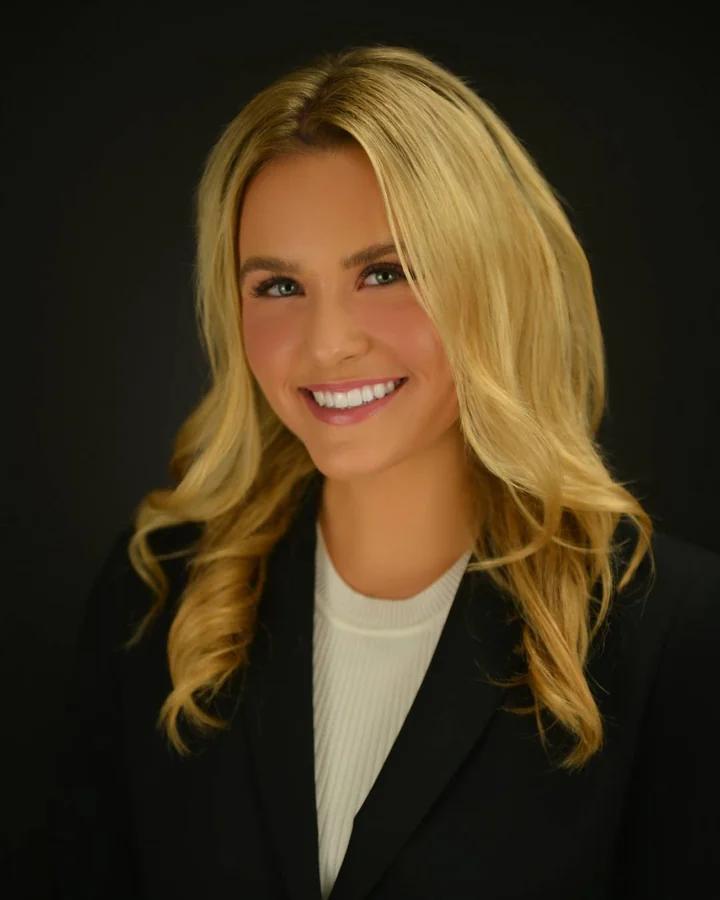 Professional headshot in a black blazer with a dark studio background